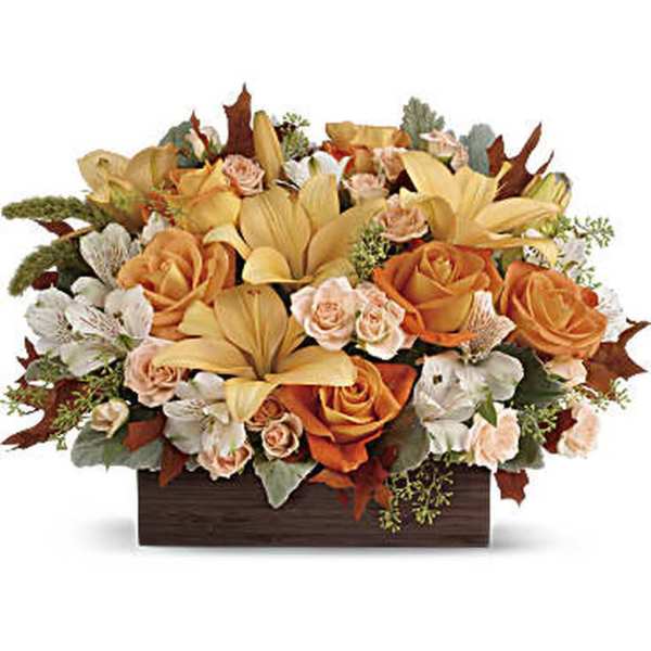 Low centerpiece of orange roses, yellow lilies, and white blooms in a dark rectangular container