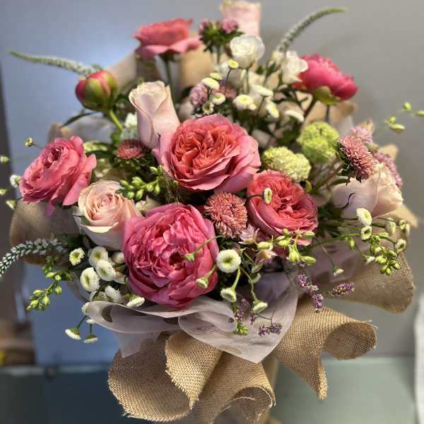 Bouquet of pink roses and small white flowers wrapped in burlap