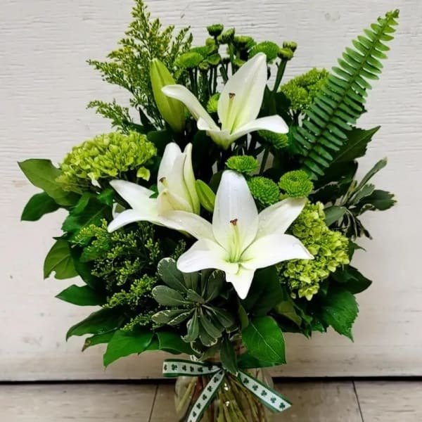 White lilies and green flowers arranged in a glass vase