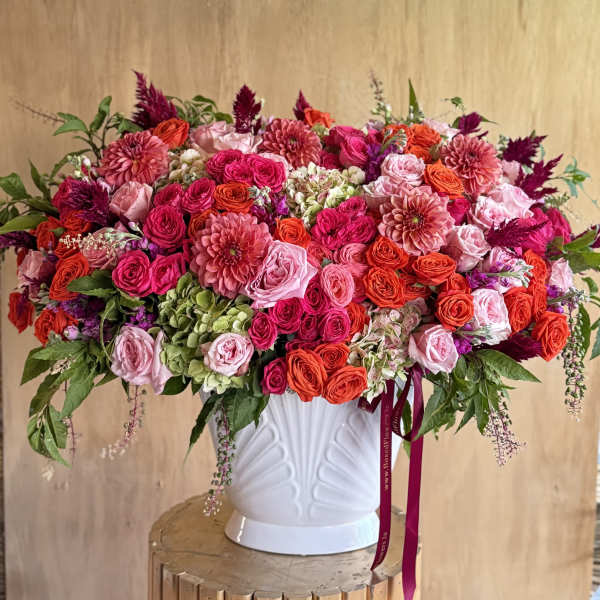 Large pink and orange floral arrangement in a white vase