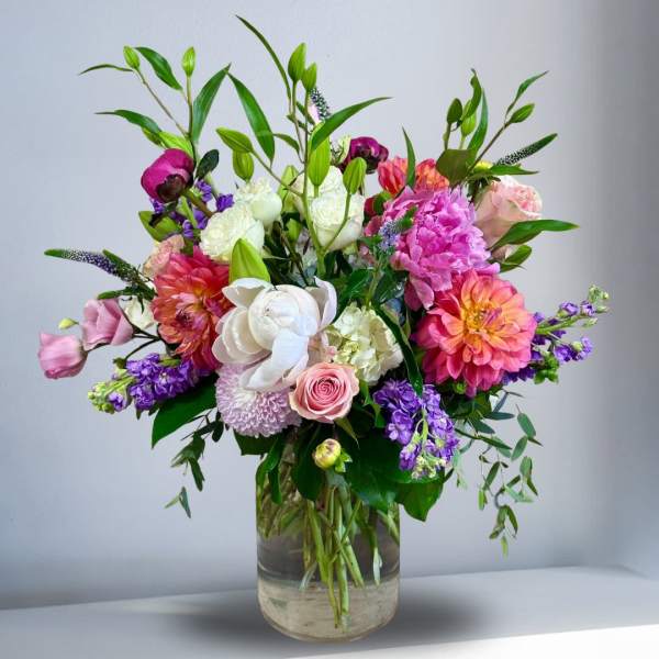 Tall arrangement of pink, peach, white and purple mixed flowers in a clear glass vase