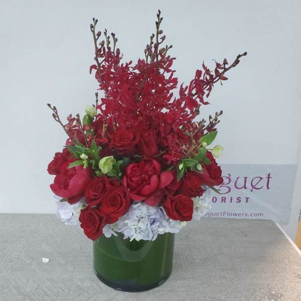 Red roses and orchids arranged in a green glass vase