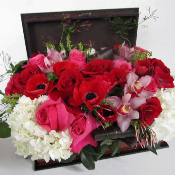 Mixed bouquet of red and pink roses with white hydrangeas and orchids in a dark box