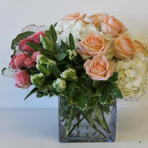 Bouquet of peach and pink roses with white hydrangeas in a square glass vase