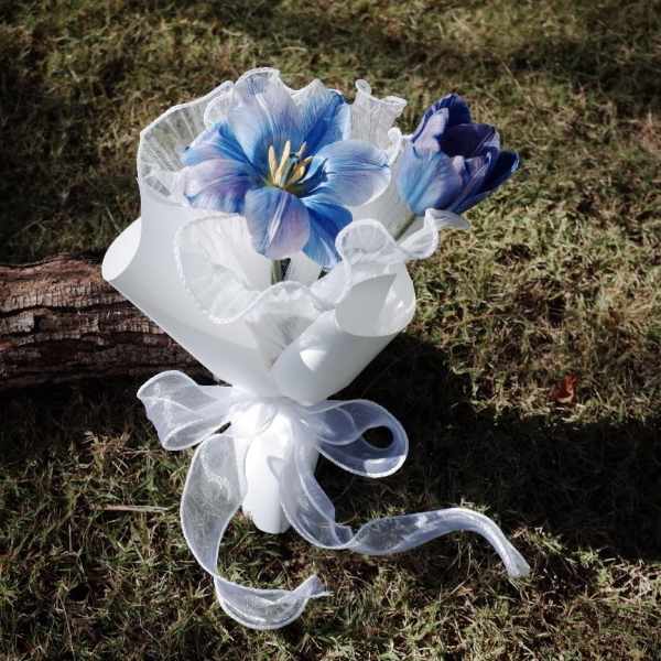 Small bouquet of blue flowers wrapped in white paper with a sheer ribbon