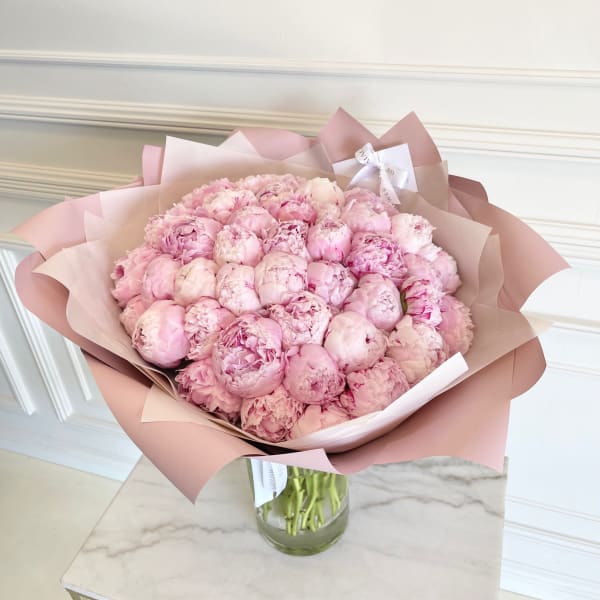 Bouquet of pale pink peonies wrapped in blush paper in a glass vase