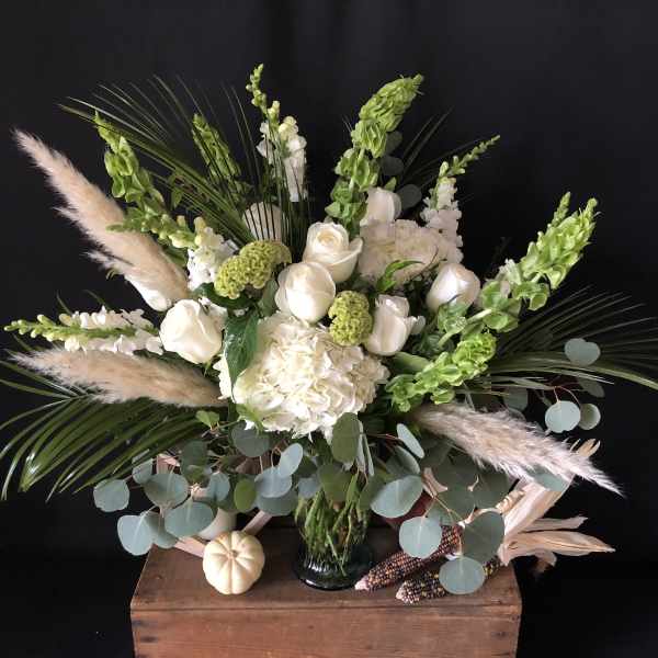 White floral arrangement in a glass vase with green accents and pampas grass
