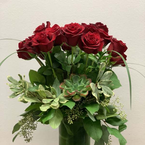 Red roses arranged in a tall green glass vase with mixed greenery.
