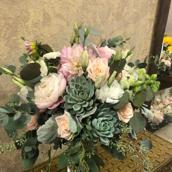 Bouquet of blush roses, pale pink blooms, and succulents in a glass vase