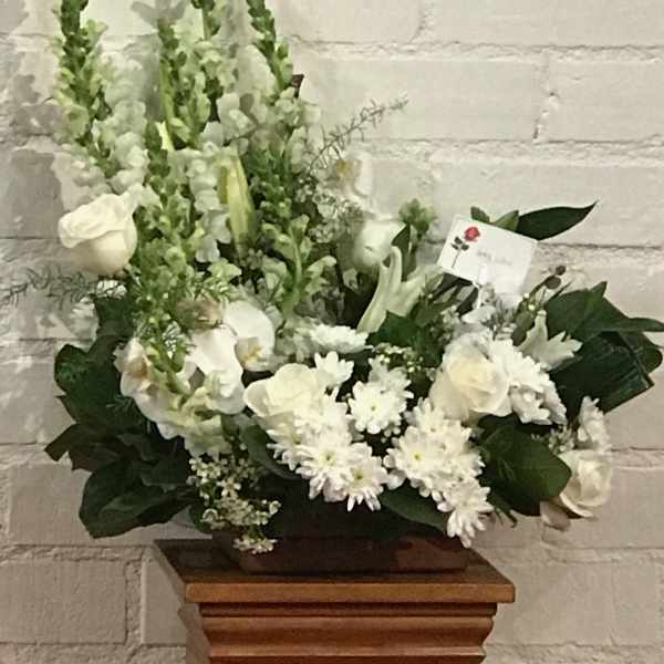 White floral arrangement with roses, lilies, and snapdragons in a low container