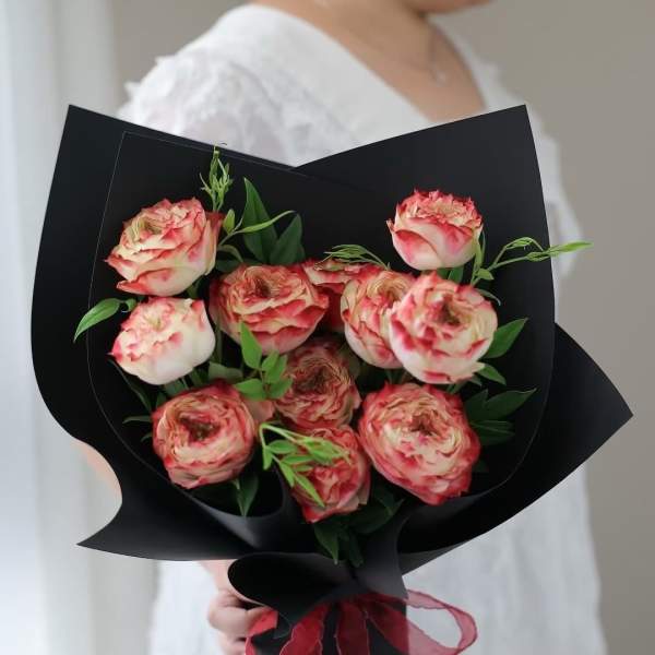 Bouquet of pink-and-cream roses wrapped in black paper with a red ribbon