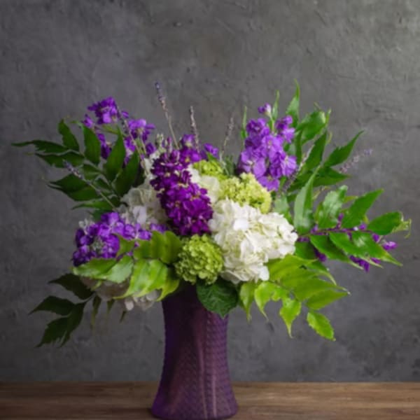 Purple and white floral arrangement in a tall purple vase