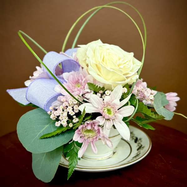 Small pastel flower arrangement in a white cup on a saucer