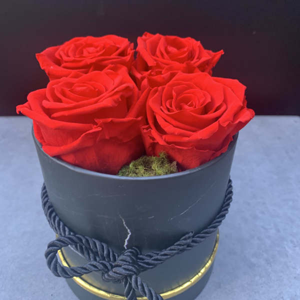 Four red roses in a black hatbox with a rope tie
