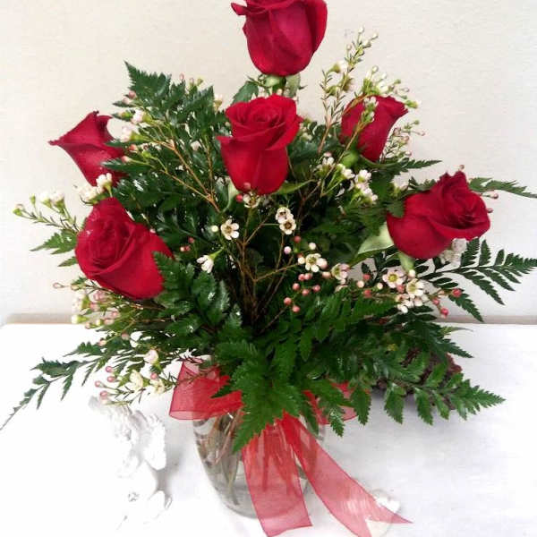 Red roses arranged in a clear glass vase with greenery and a red ribbon
