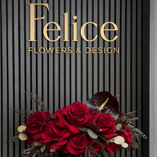 Red rose arrangement in a black hatbox with dark foliage