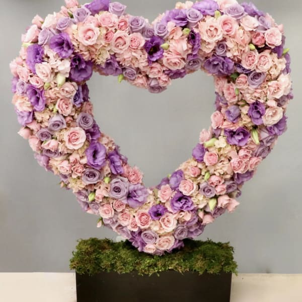 Heart-shaped floral arrangement in pink and purple roses on a moss base
