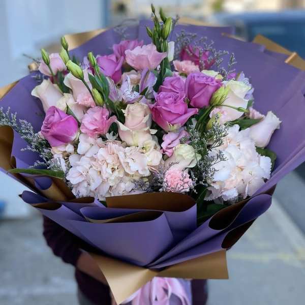 Bouquet of pink and white roses with pale hydrangeas wrapped in purple paper