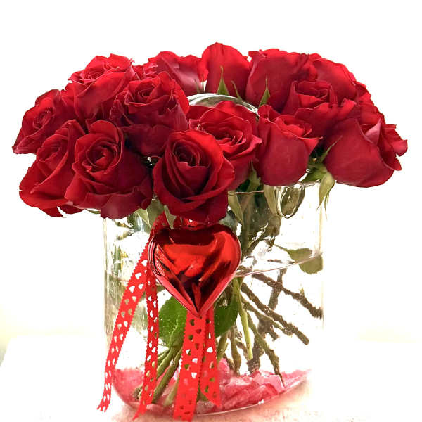 Red roses in a clear glass vase with a red heart ornament and ribbon