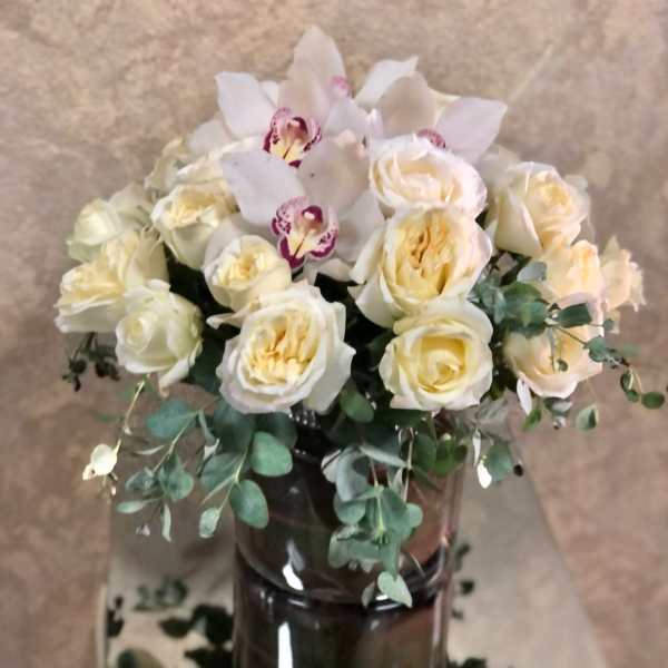 Cream roses and white orchids arranged in a dark glass vase