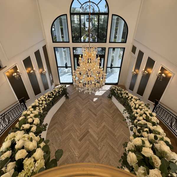 White rose arrangements line a grand staircase beneath a chandelier.