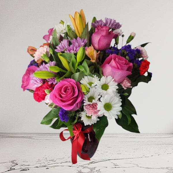 Mixed bouquet of pink roses, lilies, and daisies in a red vase