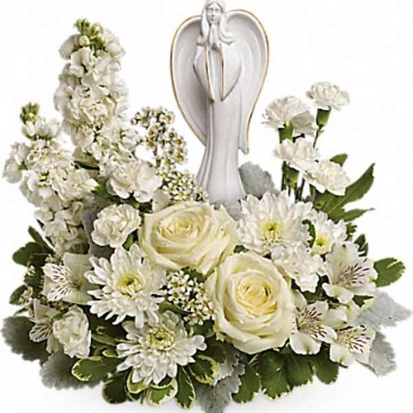 Low white flower arrangement with roses, carnations, and an angel figurine in the center.