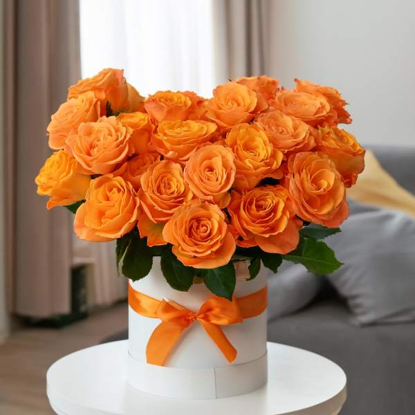 Orange roses arranged in a white hat box with an orange ribbon