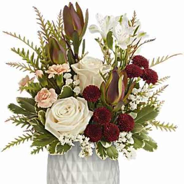 Compact arrangement of white roses, burgundy mums, and peach carnations in a white pot on a wooden stand.