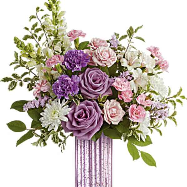 Tall bouquet of purple roses, pink spray roses, and white flowers in a ribbed lavender glass vase