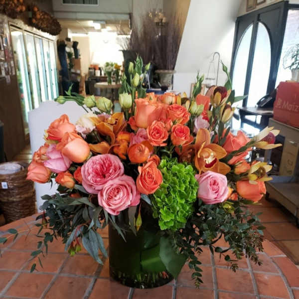 Large bouquet of peach and pink roses with orange orchids in a vase