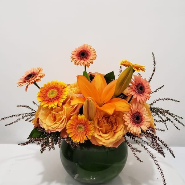 Orange and peach flowers arranged in a green glass vase