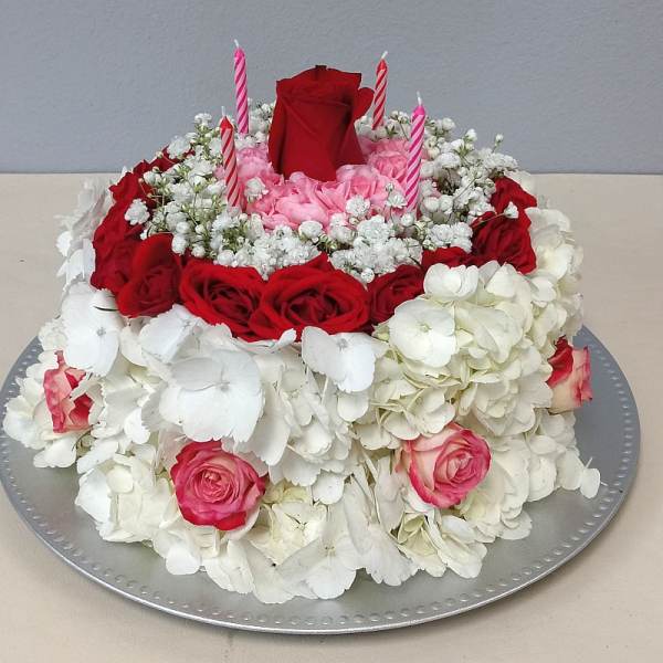 Round floral cake with red and pink roses and white hydrangeas, topped with candles