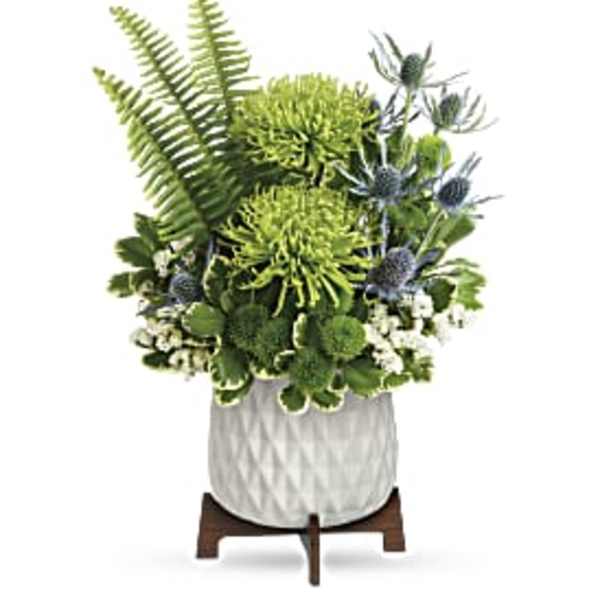 Modern green and blue floral arrangement with spider mums, fern fronds, and thistle in a white pot on wooden stand