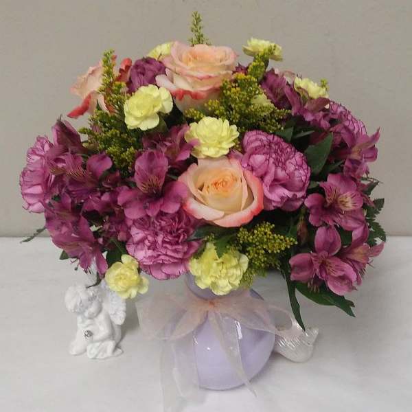 Mixed bouquet of pink and yellow flowers in a lavender vase with a ribbon