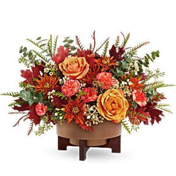 Autumn floral arrangement with orange roses and red blooms in a low container