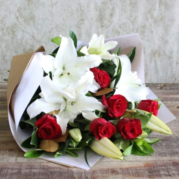 Bouquet of white lilies and red roses wrapped in paper