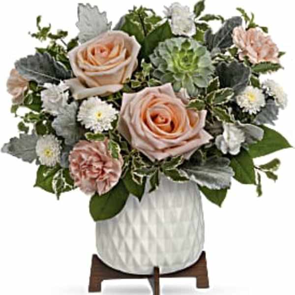 Compact arrangement of peach roses, carnations, and white mums in a white ceramic pot on a wooden stand.