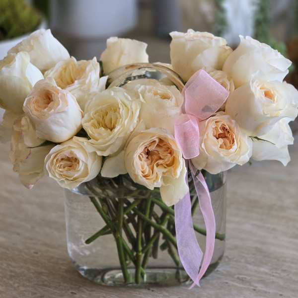 Cream roses in a clear glass vase with a pink ribbon