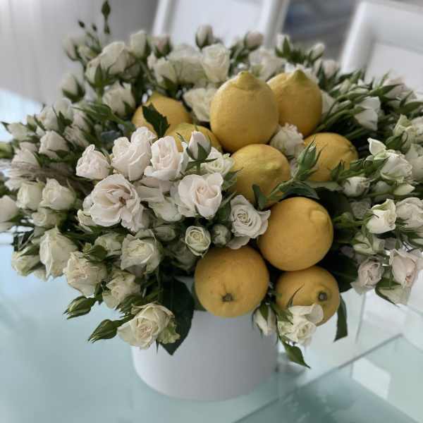 White roses arranged with lemons in a white vase
