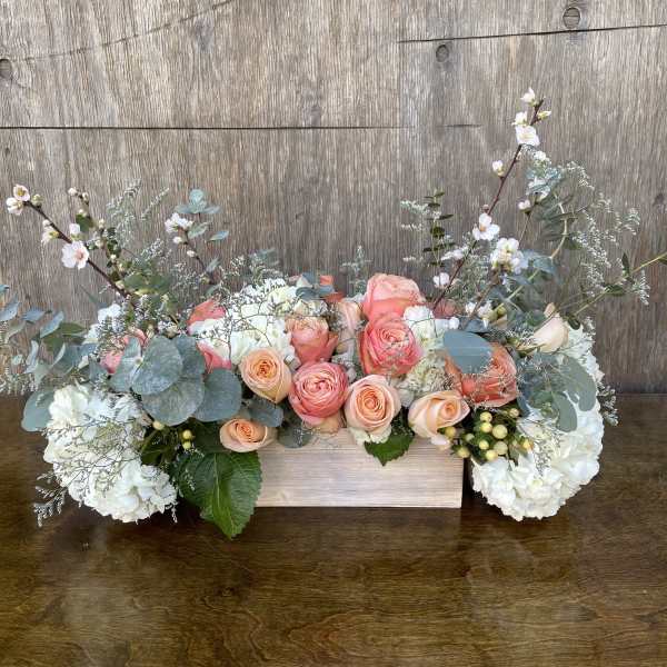 Low floral arrangement of peach and white roses with white hydrangeas in a wooden box