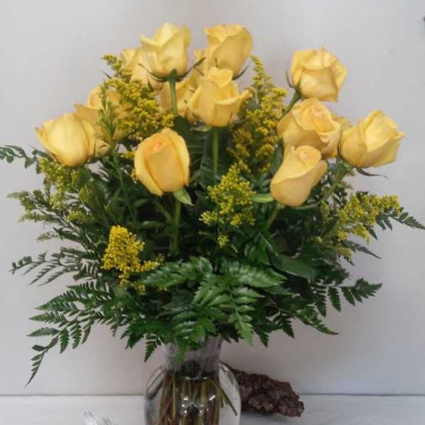 Yellow roses arranged in a clear glass vase with greenery