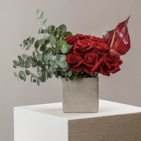 Red roses in a square vase with eucalyptus and a red anthurium