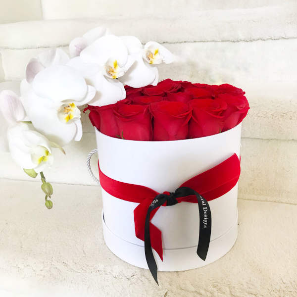 Red roses in a white hat box with white orchids draped over the side