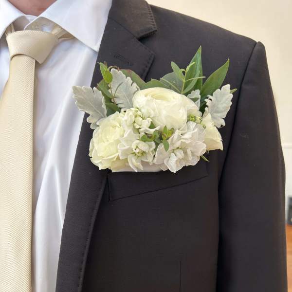 White boutonniere on a dark suit jacket with a cream tie