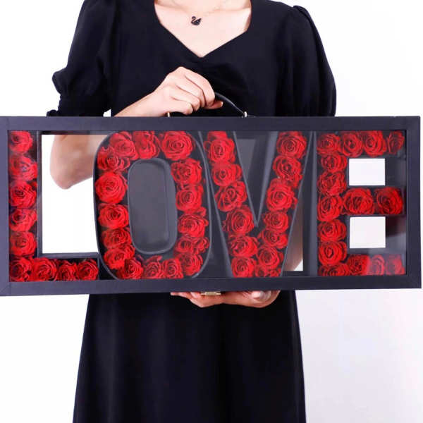 Framed LOVE sign filled with red roses, held by a person in black