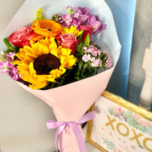 Bouquet of sunflowers, roses, and purple flowers wrapped in pink paper