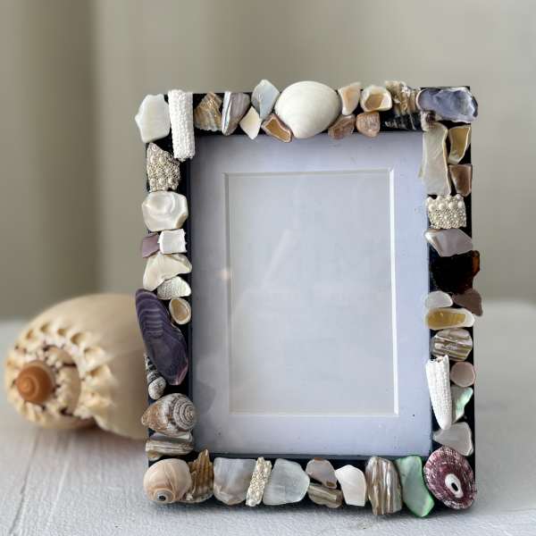 Shell-covered photo frame on a table with a seashell ornament behind it