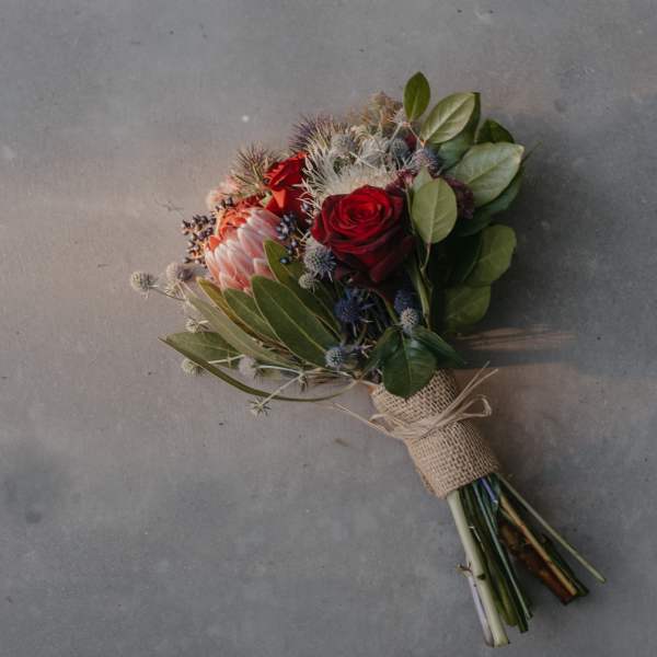 Hand-tied bouquet with red roses and a pink protea