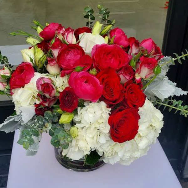 Low glass vase of red and hot pink roses with white hydrangeas on a white pedestal